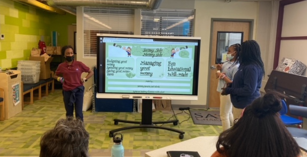 Syracuse Academy of Science middle school PBL students pitch their interactive game designed to teach elementary students about being strong money managers to Empower Federal Credit Union’s Financial Education Officer, Cheryl Welles.